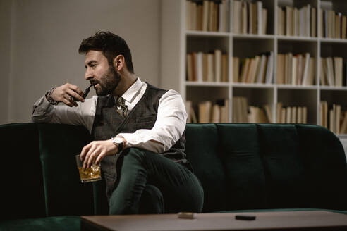 Porträt eines bärtigen Mannes, der sich auf dem Sofa mit einer Pfeife und einem Glas Whiskey entspannt - GIOF10384