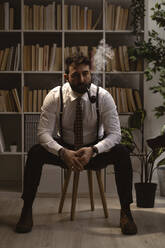Porträt eines bärtigen Mannes, der auf einem Hocker sitzt und Pfeife raucht - GIOF10400
