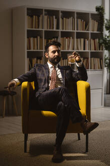 Porträt eines gut gekleideten Mannes, der in einem Sessel sitzt und eine Zigarre und ein Glas Whiskey genießt - GIOF10401