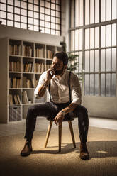 Portrait of bearded man sitting on stool and smoking cigar - GIOF10412