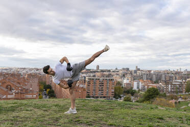 Männlicher Akrobat übt Kickboxen gegen den bewölkten Himmel über der Stadt - GGGF00573