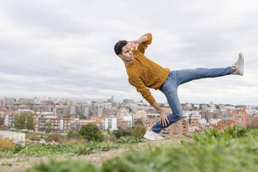 Mann tut akrobatische Tätigkeit auf dem Hügel in der Stadt gegen bewölkten Himmel - GGGF00581