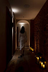 Junge Kundin im Bademantel geht in einem dunklen Korridor im Wellnessbereich spazieren - OCMF01889