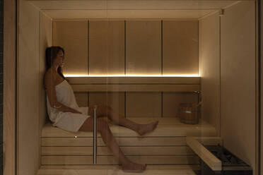 Junge weibliche Kundin sitzt in der Sauna im Wellnessbereich - OCMF01894