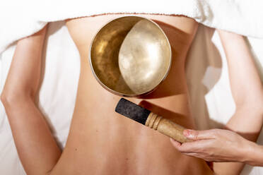 Therapist holding mallet by rin gong on female customer's back at health spa - OCMF01930