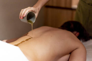Reife Therapeutin gießt Massageöl auf den Rücken einer Frau im Schönheitssalon - OCMF01935