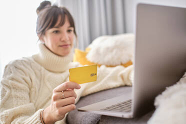 Woman shopping online with credit card through laptop at home - AODF00105