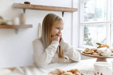 Smiling girl looking at cookies on table in kitchen - EYAF01442