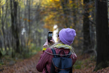 Frau fotografiert Bäume mit Smartphone im Winter im Wald - CHPF00740