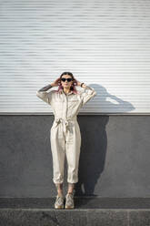 Stilvolle junge Frau mit Sonnenbrille an der Wand an einem sonnigen Tag - VPIF03354
