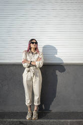 Hipster female with arms crossed wearing sunglasses against wall on sunny day - VPIF03356