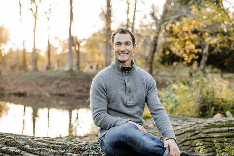 Smiling mid adult man sitting on log in public park stock photo