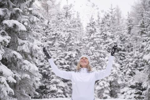 Glückliche ältere Frau genießt Schnee gegen Wald während der Ferien, lizenzfreies Stockfoto