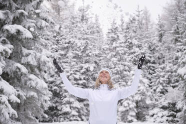 Happy senior woman enjoying snow against forest during vacations - MRF02425