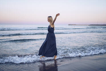 Woman with arms outstretched walking in water at  Platja de Llevant beach - RSGF00465