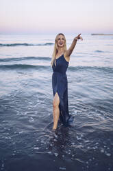 Smiling woman pointing while standing in water at Platja de Llevant beach - RSGF00467
