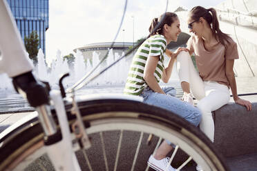 Cheerful friends sitting on retaining wall while spending weekend together in city - ABIF01283