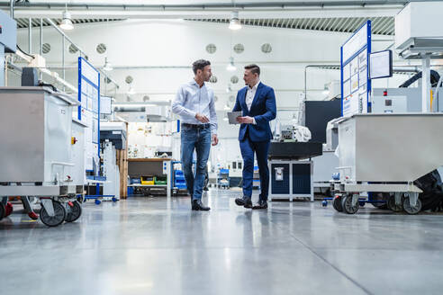 Männlicher Berufstätiger im Gespräch mit einem Mitarbeiter beim Spaziergang in einer Fabrik - DIGF13533