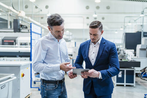 Geschäftsmann mit männlichem Kollegen bei der Arbeit an einem digitalen Tablet in einer Fabrik - DIGF13535
