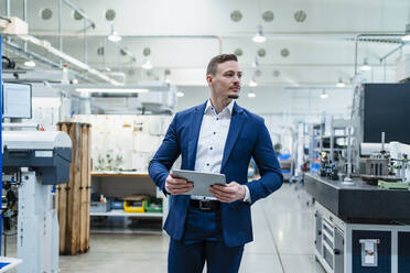 Businessman holding digital tablet while looking around in factory - DIGF13540