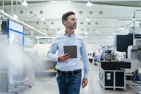 Businessman holding digital tablet while walking at industry - DIGF13543