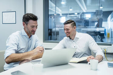 Smiling businessman with male coworker working on laptop in board room at factory - DIGF13554