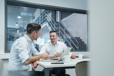 Smiling male professional looking at male colleague in boardroom at industry - DIGF13555