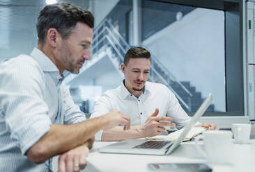 Männliche Mitarbeiter diskutieren über Strategie am Laptop im Sitzungssaal eines Fabrikbüros - DIGF13556