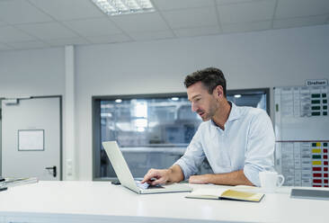 Male professional working on laptop while sitting in board room at factory office - DIGF13559