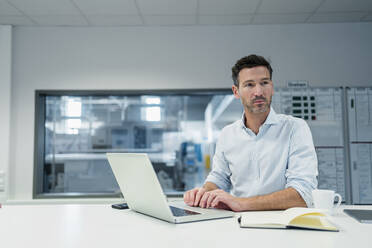 Mature businessman with laptop contemplating in board room at industry office - DIGF13560