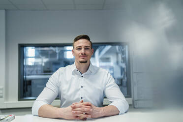 Handsome businessman with hand clasped in board room at factory office - DIGF13563