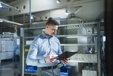 Male professional looking at file in factory by rack - DIGF13565