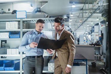 Geschäftsmann mit männlichem Mitarbeiter diskutiert über Datei-Dokument, während in der Industrie stehen - DIGF13569