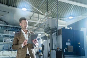 Mature businessman using digital tablet against machines at factory - DIGF13572