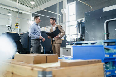 Business people discussing while surrounded by machinery in factory - DIGF13587