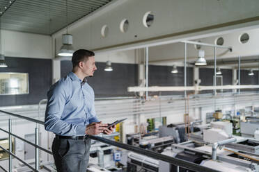 Geschäftsmann mit digitalem Tablet mit Blick auf eine Fabrikhalle - DIGF13604