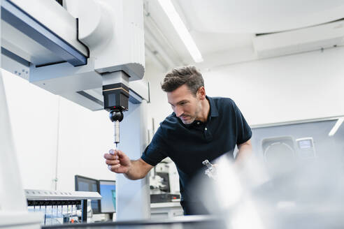 Älterer männlicher Techniker, der einen Bohrer in einer Maschine in einer Fabrik befestigt - DIGF13617