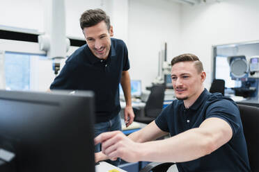 Ein lächelnder männlicher Ingenieur zeigt einem Kollegen in einem Fabrikbüro einen Computer - DIGF13622