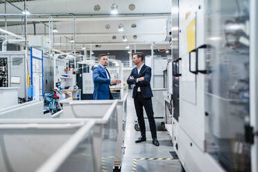 Businessman with arms crossed listening to male coworker in industry - DIGF13637