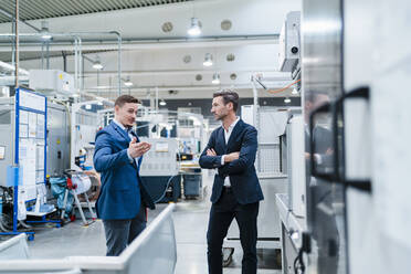 Geschäftsleute diskutieren, während sie in einer von Maschinen umgebenen Fabrik stehen - DIGF13638