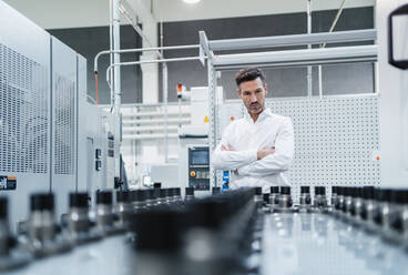 Mature businessman with arms crossed examining machinery equipment in industry - DIGF13643