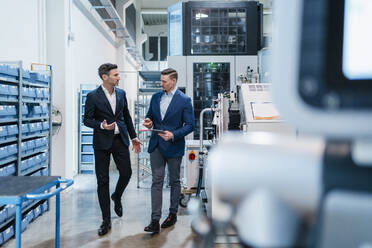 Male coworkers with digital tablet discussing while walking in industry - DIGF13647