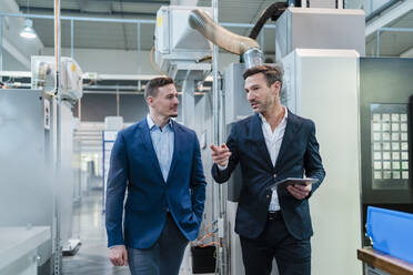 Businessman talking with male colleague walking in factory - DIGF13648