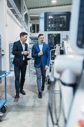 Male colleagues discussing while looking at machinery equipment in industry - DIGF13649