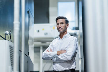 Mature businessman with arms crossed looking away while standing in factory - DIGF13660