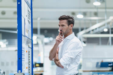 Mature businessman contemplating while checking plan board at factory - DIGF13662