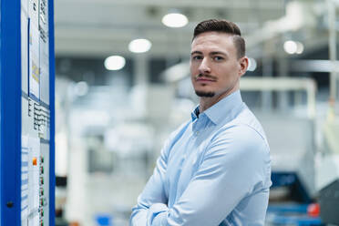 Mid adult businessman with arms crossed standing by board in industry - DIGF13664