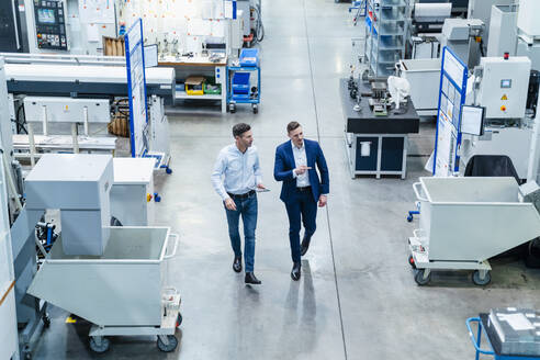 Männliche Kollegen mit digitalem Tablet, die über Maschinenausrüstung in einer Fabrik diskutieren - DIGF13666