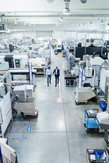 Männliche Mitarbeiter gehen in einer Fabrik, umgeben von Produktionsanlagen - DIGF13667
