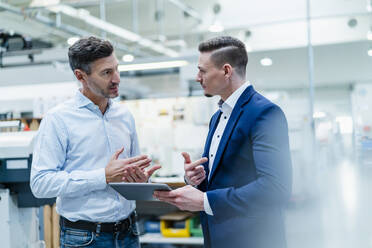 Male professionals with digital tablet having conversation while standing in factory - DIGF13669